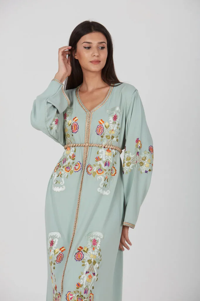 Woman wearing a pastel green Moroccan caftan with colorful floral embroidery and gold trim